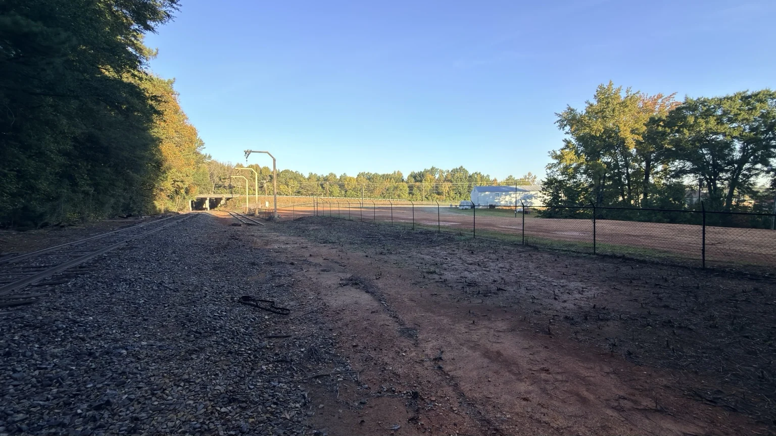 Wide view along the rail spur beside the fenced, cleared Meeting Street industrial yard