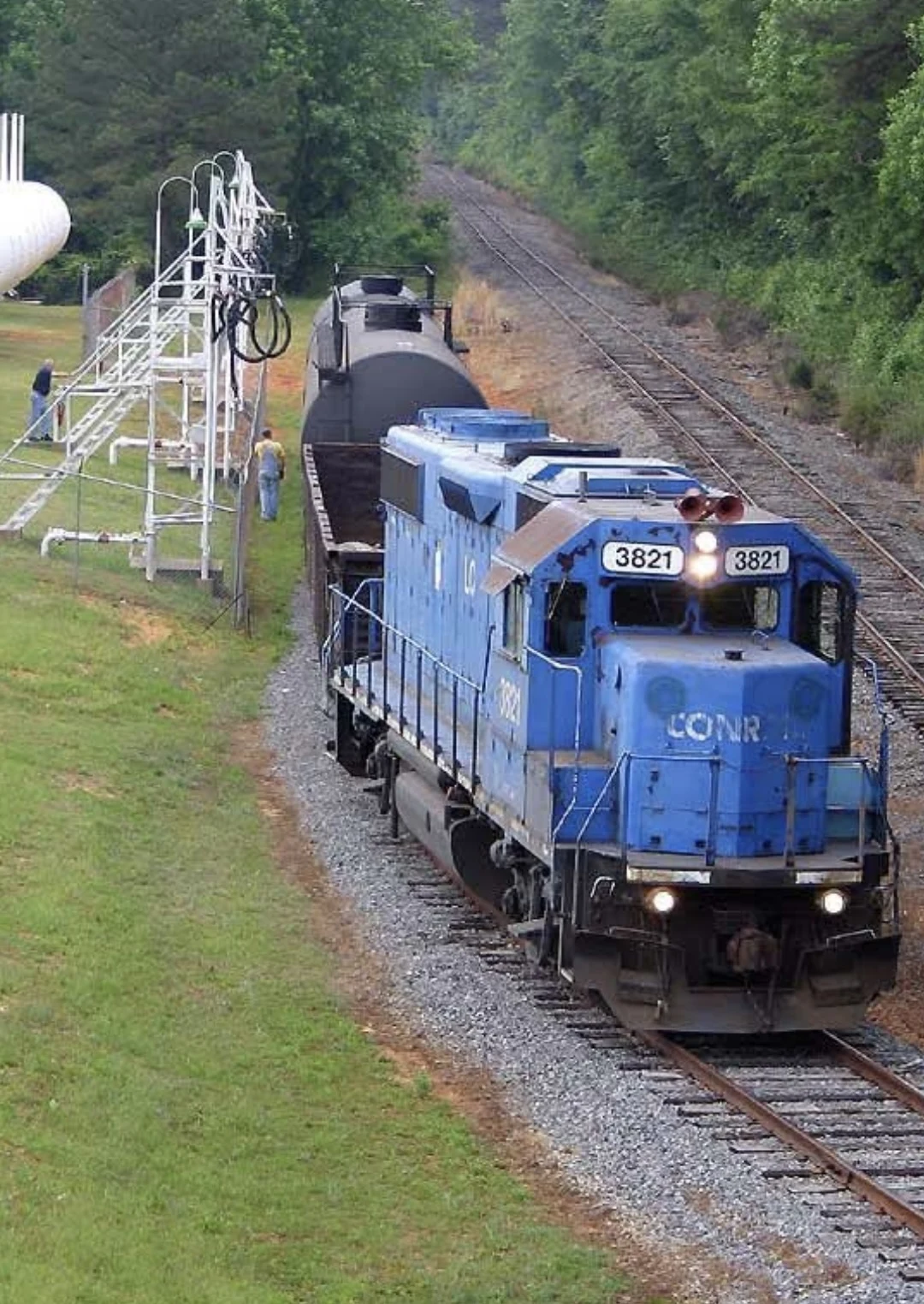 Historical owner-supplied photograph of a blue locomotive and tank car beside a rail loading area